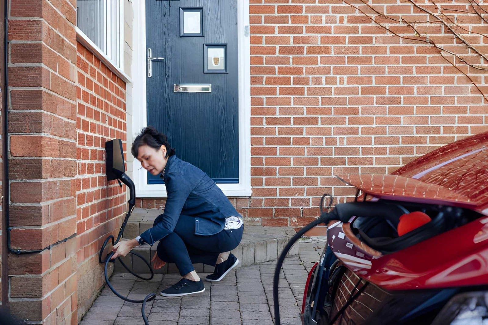 A homeowner connecting their electric car to a home EV charge point on a brick house.