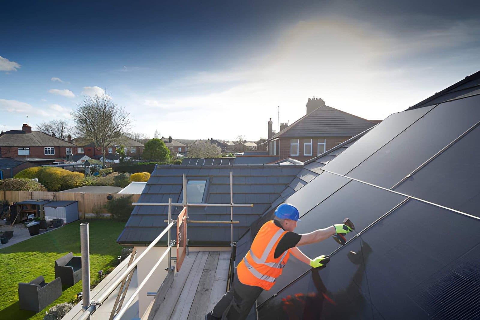 An installer in hi-vis fitting black solar PV panels on a domestic roof.